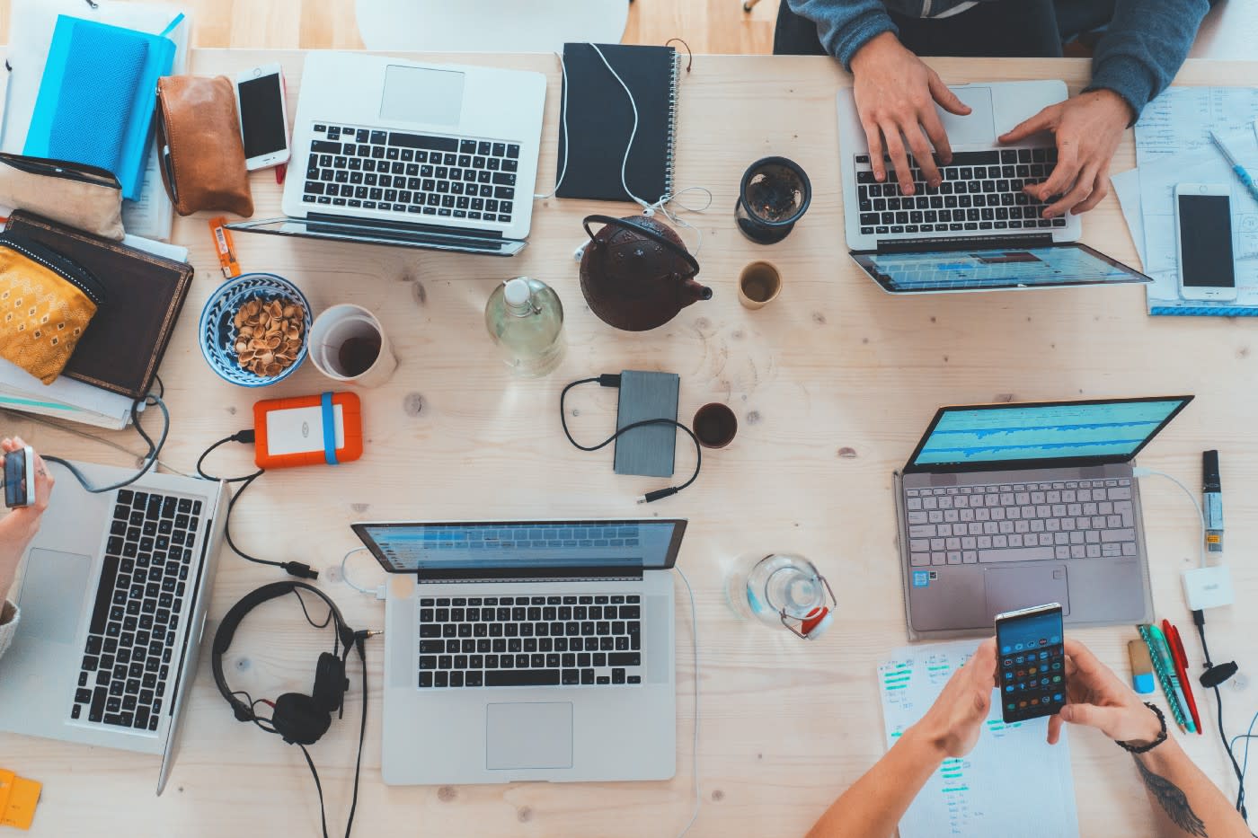 Laptops on table with hands, coffee, snacks, and headphones